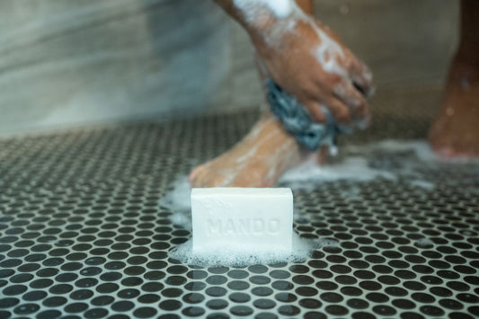 white mando bar soap on shower floor with man washing his legs in the background