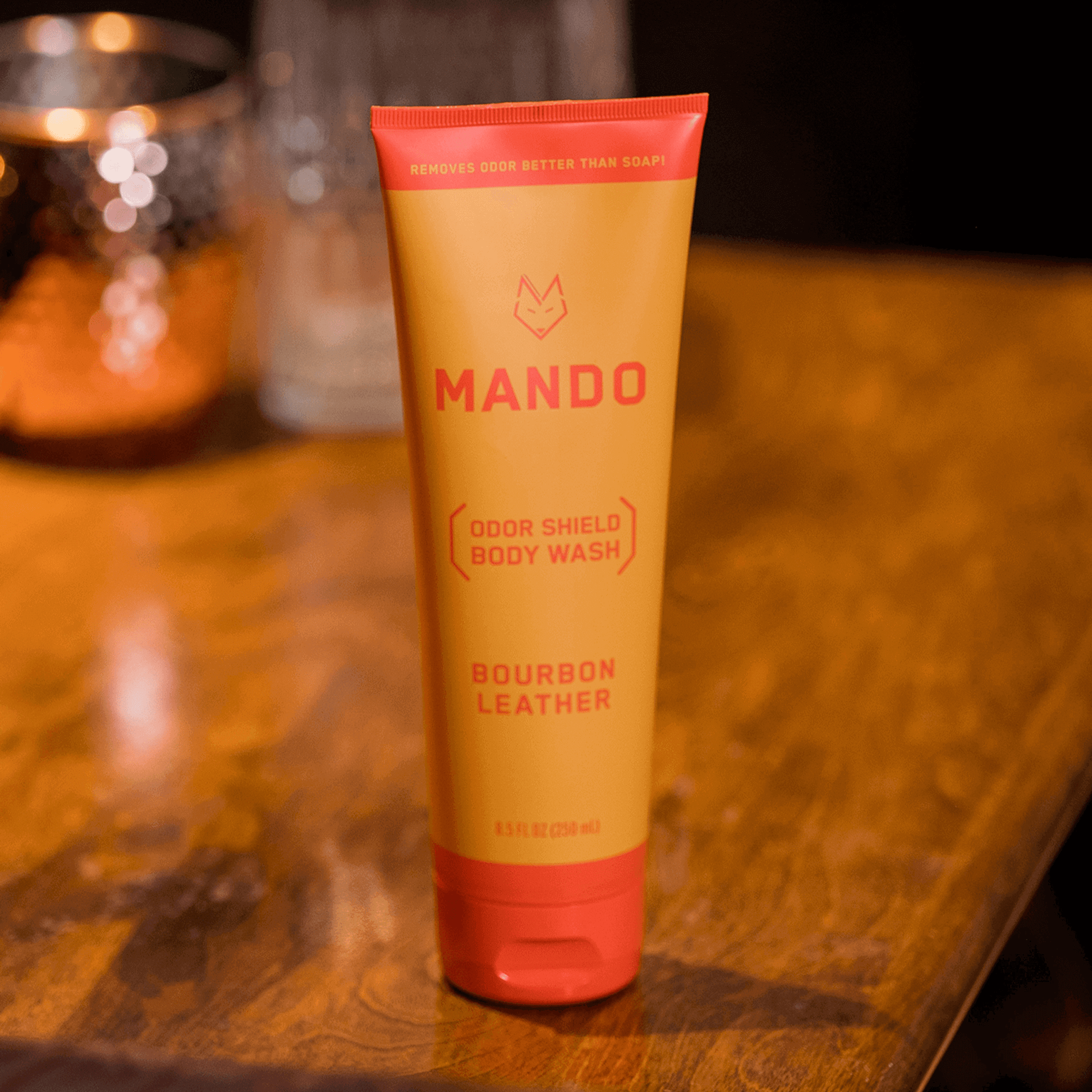 yellow orange tube of Mando body wash in bourbon leather scent sitting on a wooden table 