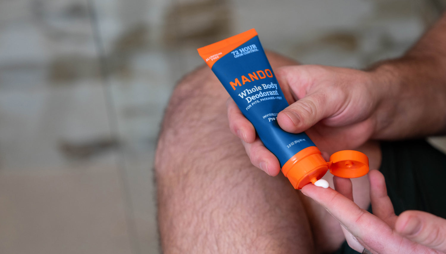 man sitting, crossing his legs and holding an open tube of Mando Pro Sport cream deodorant 