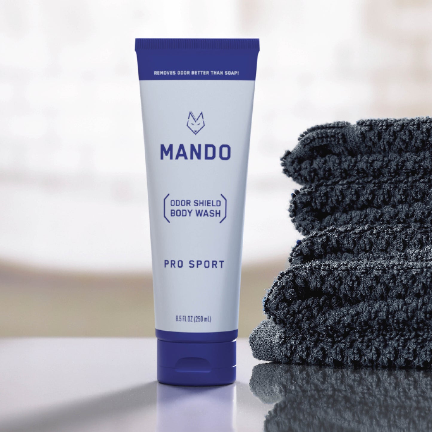 blue tube of Mando body wash in pro sport scent placed beside a stack of blue towels 